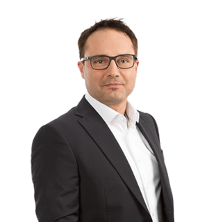 Mann im dunklen Anzug mit Brille vor hellem Hintergrund