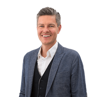 Person in Sakko lächelt in frontaler Porträtaufnahme